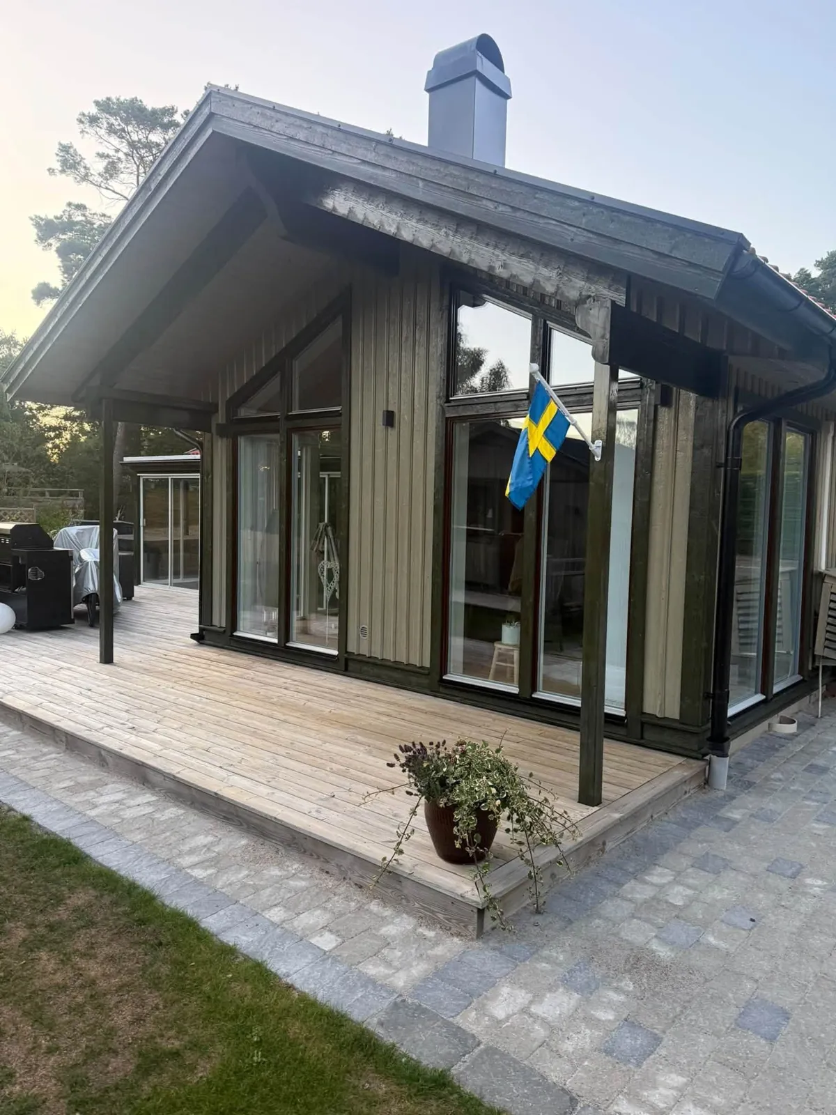 Villa med olivgrön träpanel, mörka fönsterfoder och stora fönster mot altanen