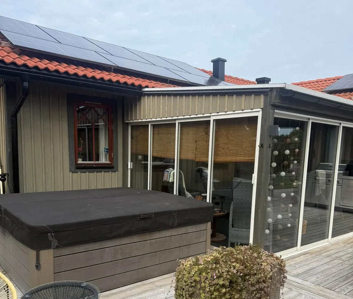 Inglasat uterum och altan vid ett hus med olivgrön panel